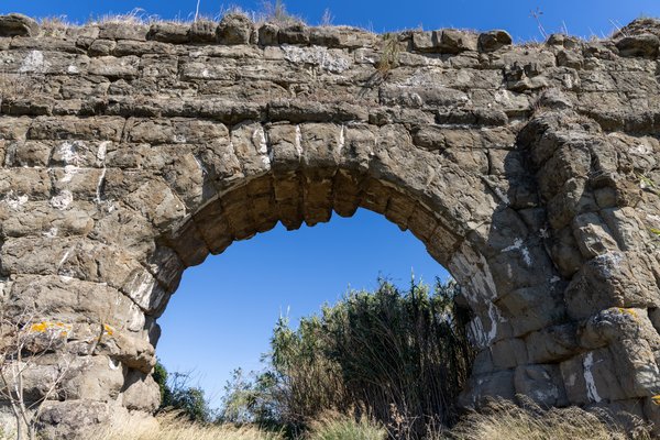 Sunlit aqueduct arch against blue sky